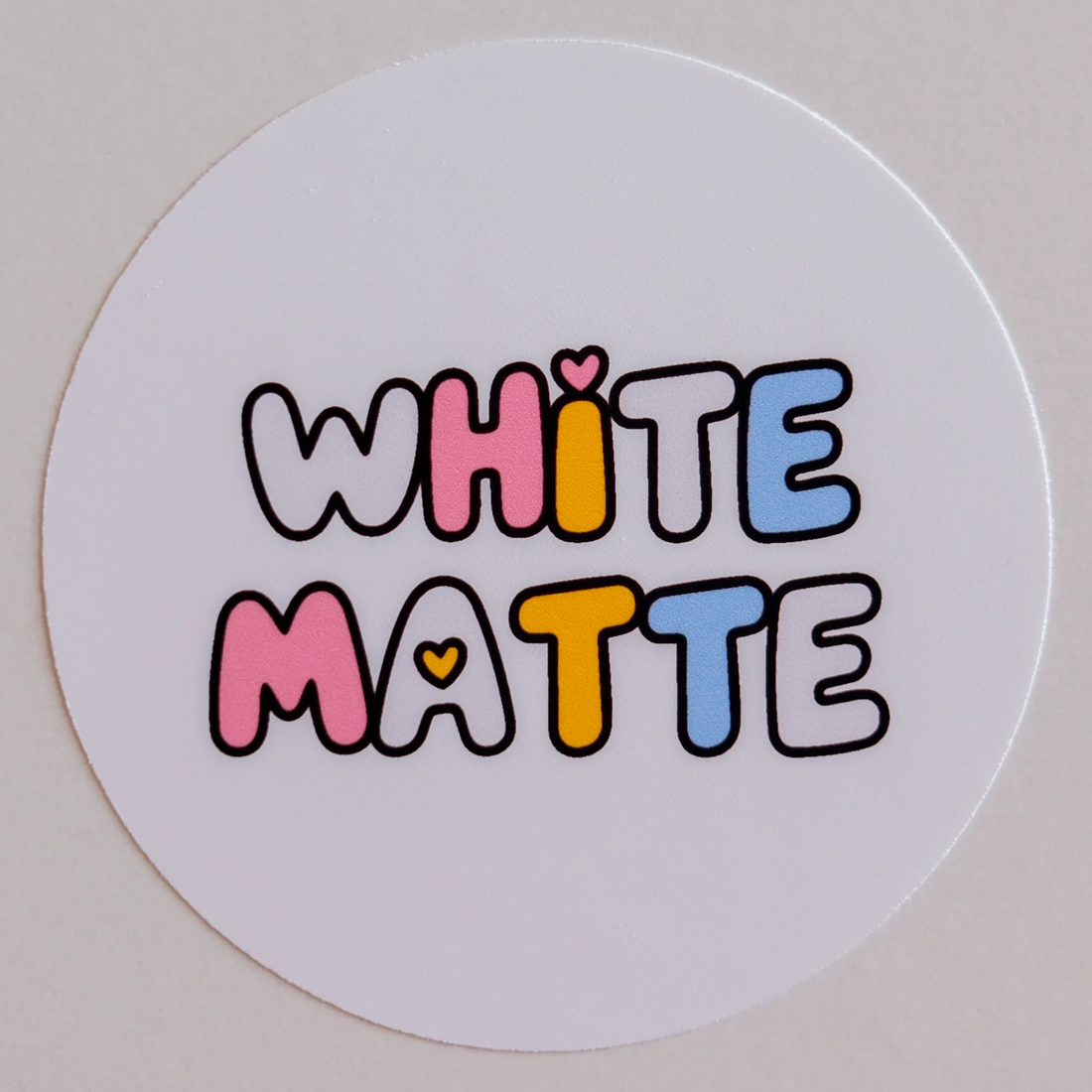 White Matte sample: a round sticker printed with WHITE MATTE in bubble letters