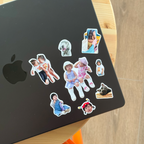 Nine Package Full stickers arranged across the lid of a black MacBook on a wood table