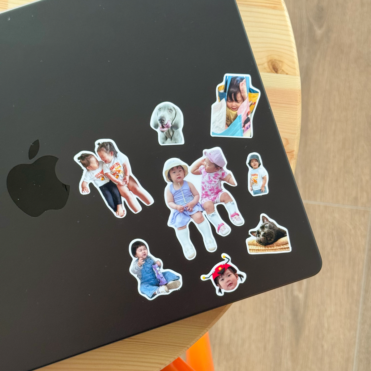 Nine Package Full stickers arranged across the lid of a black MacBook on a wood table